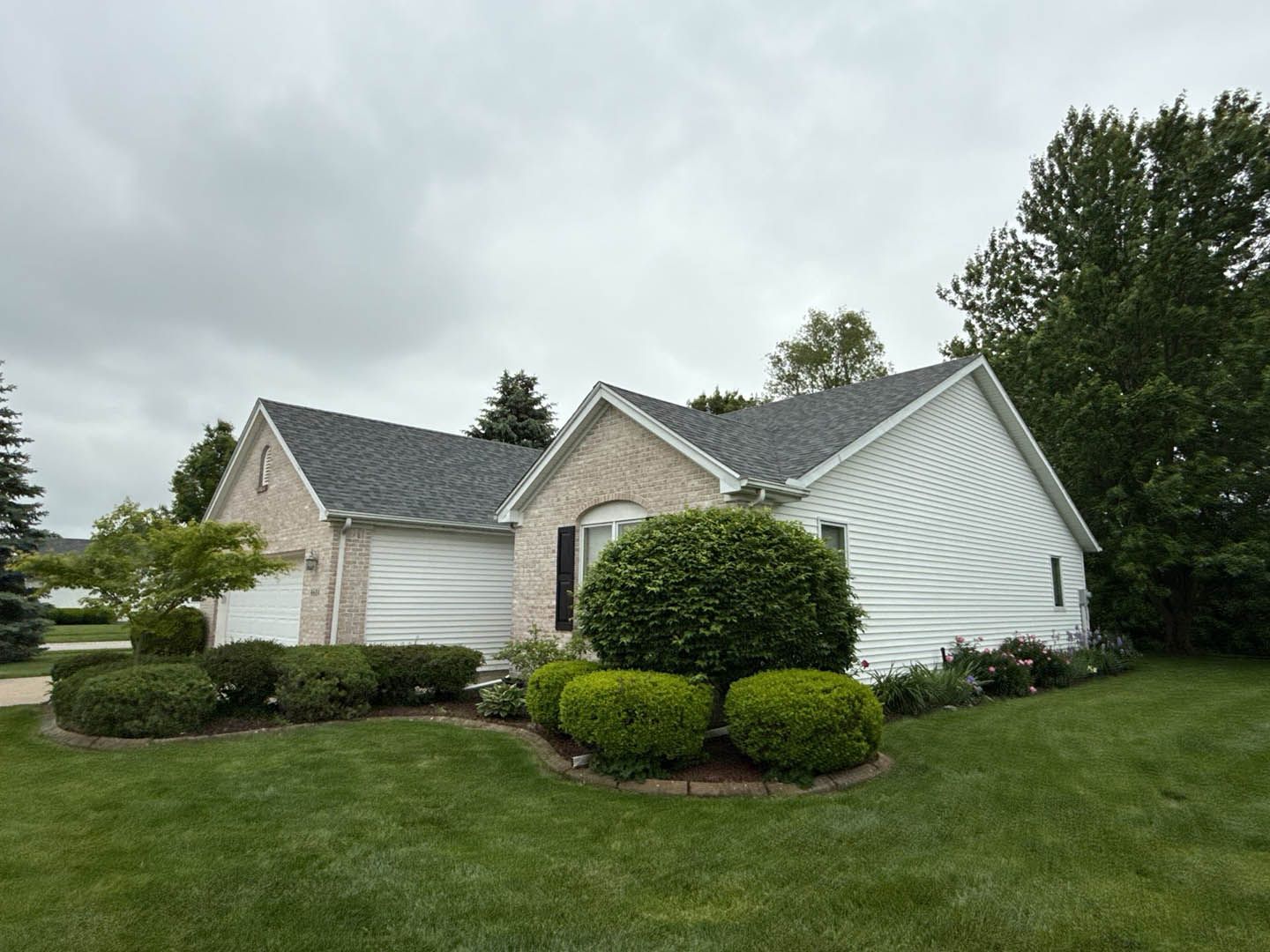 Suburban house with gray siding, manicured lawn, and trimmed shrubs under cloudy skies