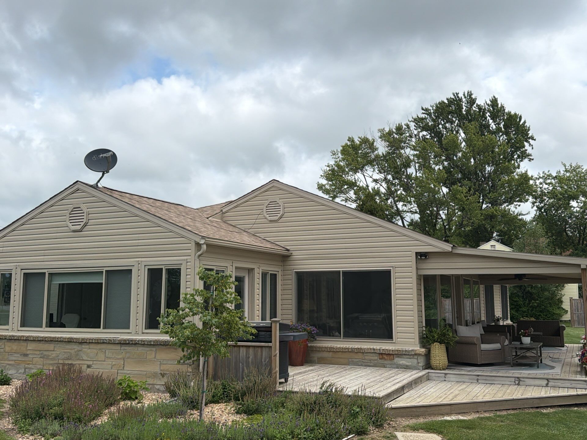 Single-story beige house with a covered patio, large windows, and a cloudy sky overhead