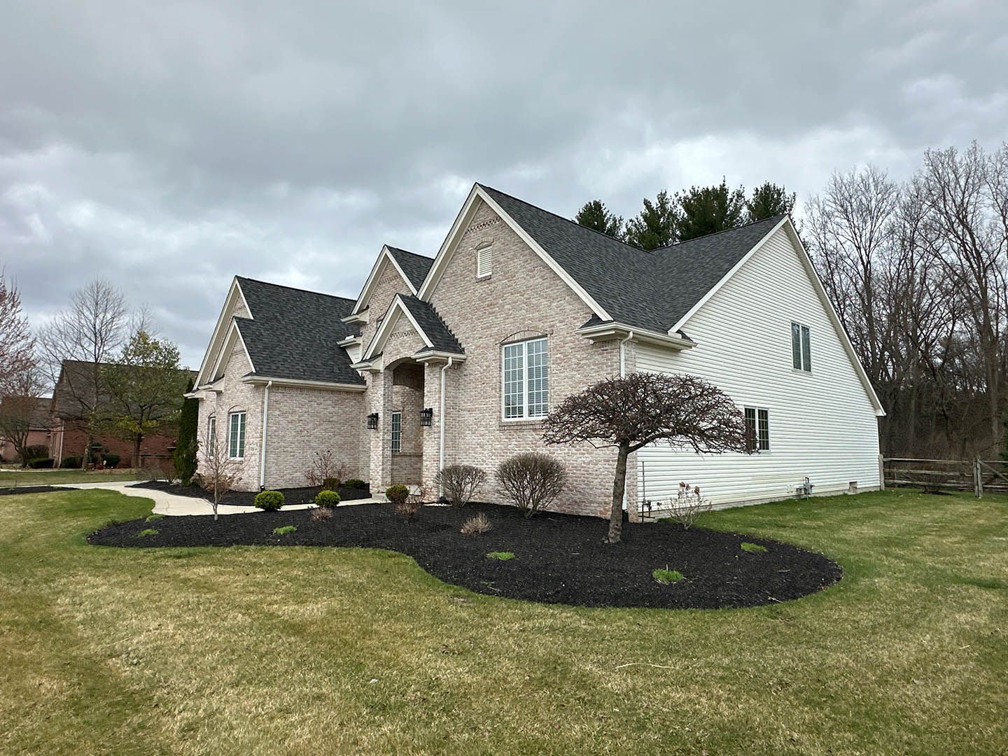 Suburban brick and white house with dark mulch landscaping and cloudy sky