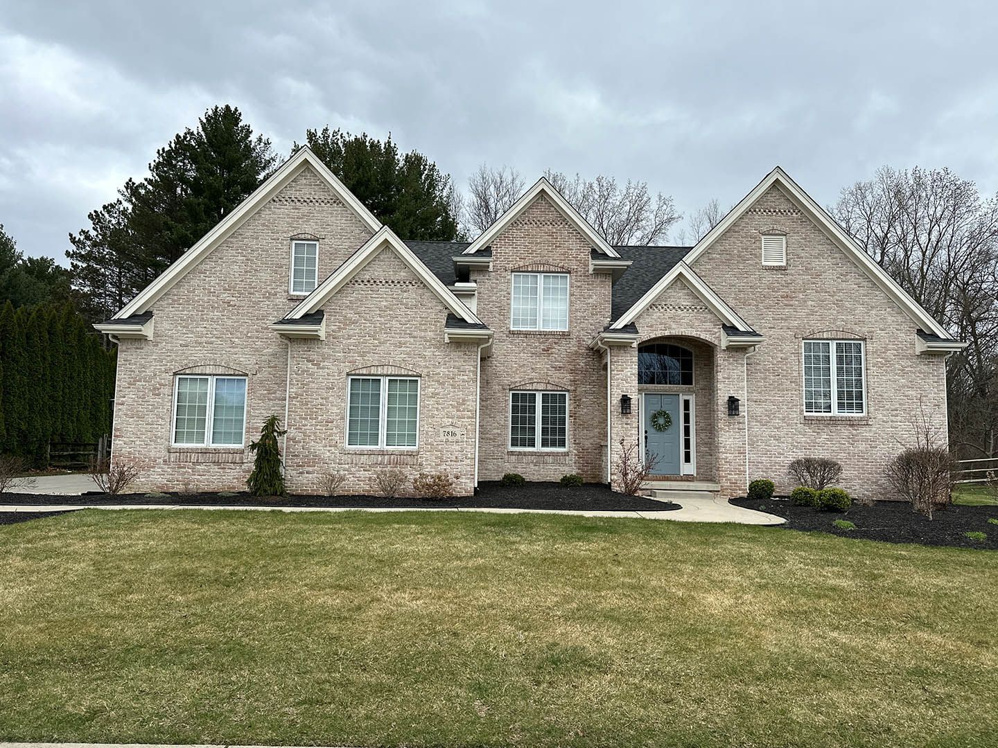 Large stone suburban house with front lawn and trees under an overcast sky