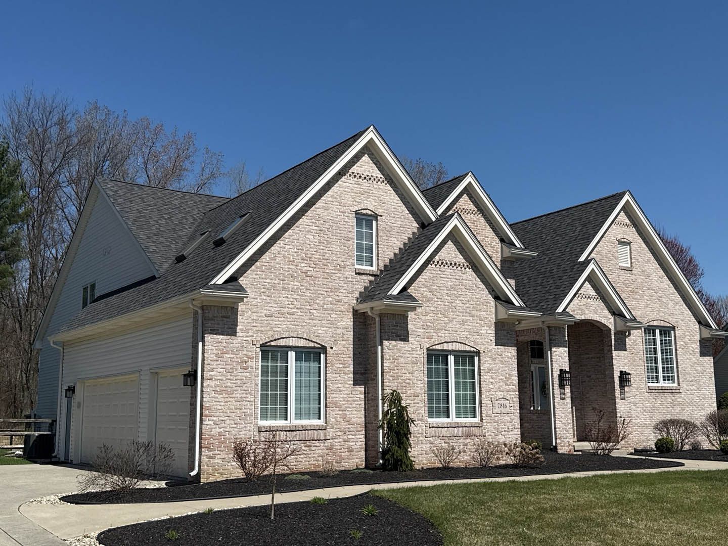 Brick suburban house with gray roof, white garage, and front porch under a clear blue sky