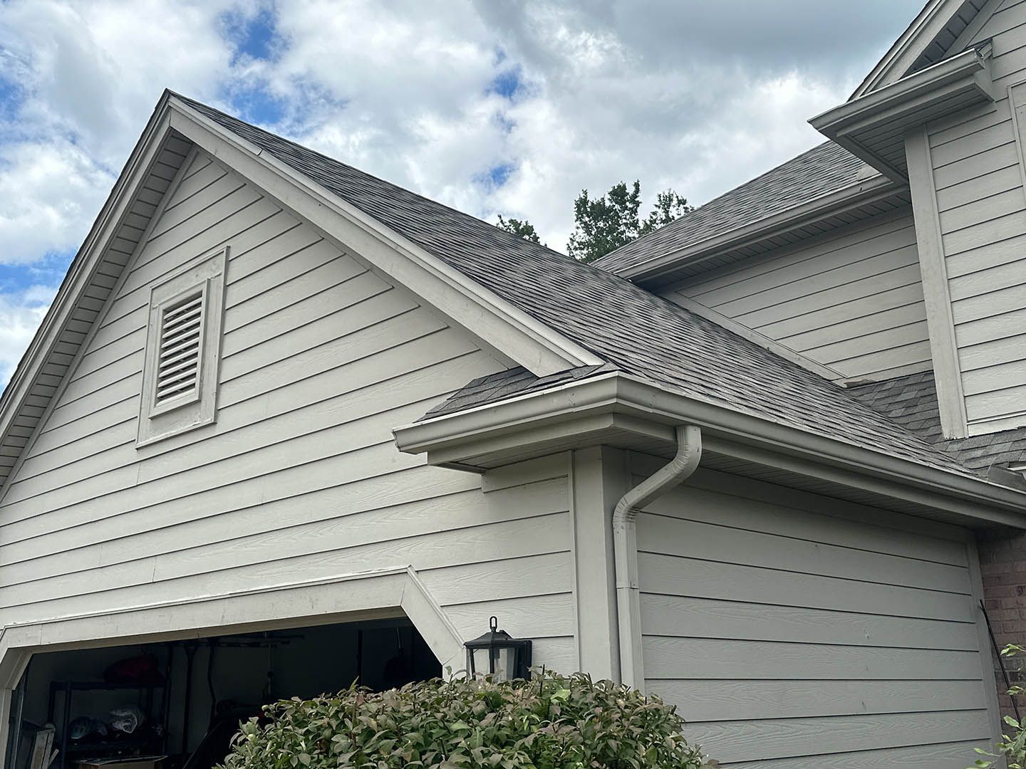 White suburban house exterior with gray roof, siding, and an attached garage under cloudy skies