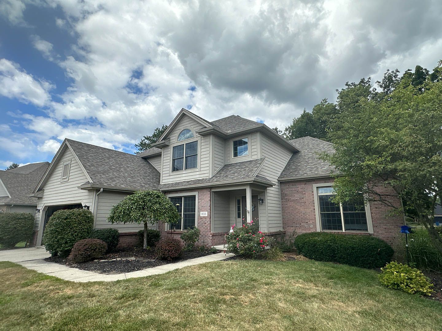 Suburban brick house with stone accents, gabled roof, and cloudy sky over a front lawn
