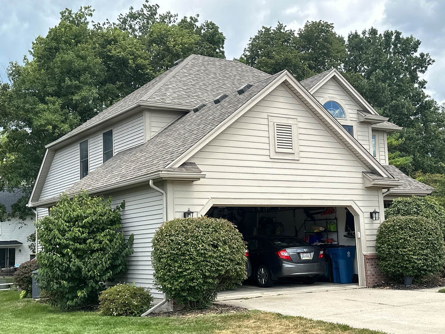 Suburban house with beige siding, gray roof, and open garage with a car inside