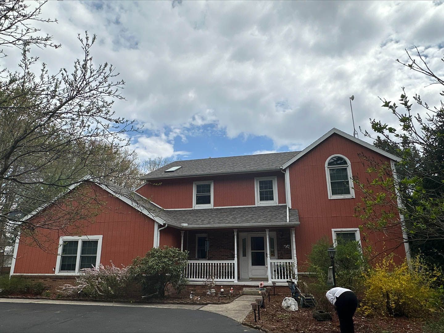 Red two-story house with white trim and cloudy sky; person kneels near the front walkway.
