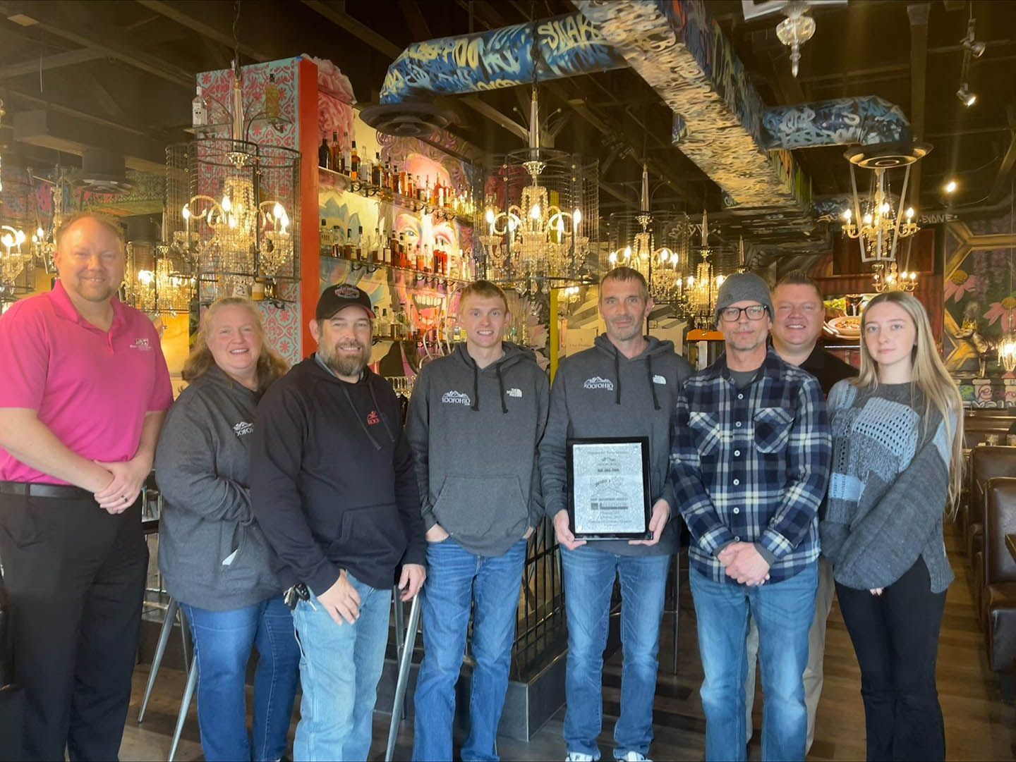 Group of people posing in a warmly lit restaurant, one holding a framed certificate.