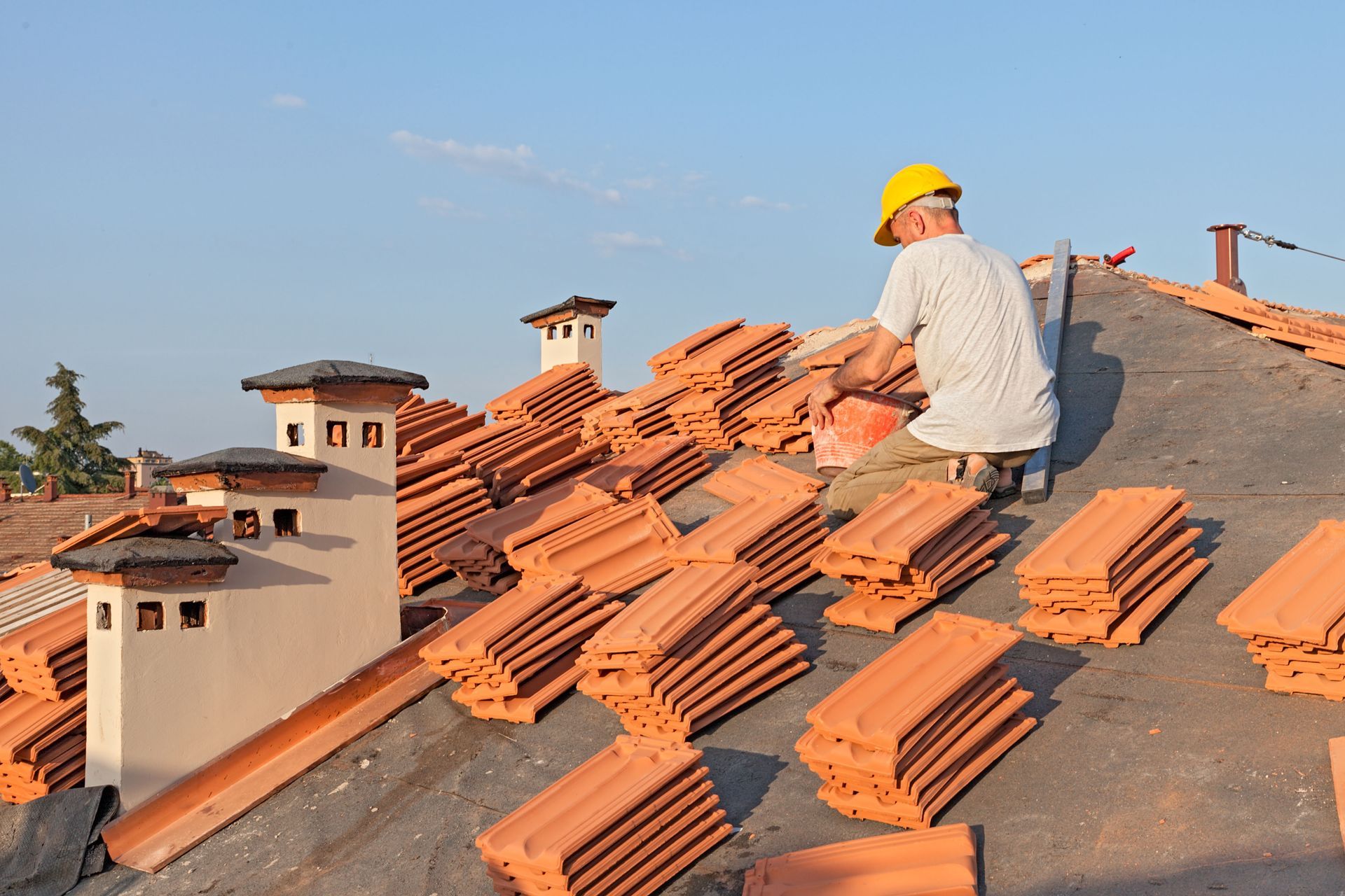 Worker installing orange roof tiles on a sloped rooftop under a blue sky