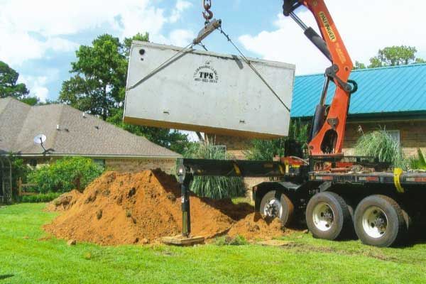 A crane is lifting a large concrete box over a pile of dirt