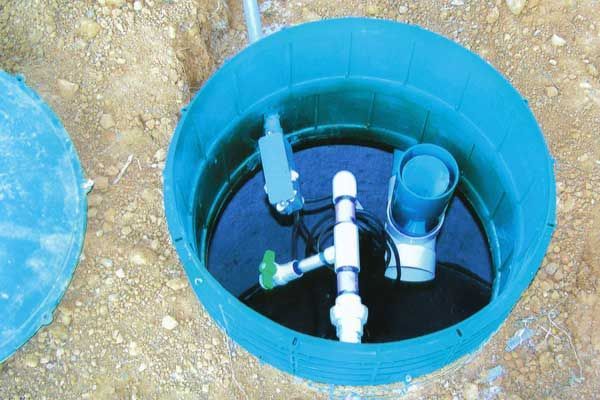 A blue barrel filled with water and pipes is sitting in the dirt.