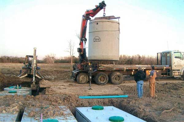 A large concrete tank is being lifted by a crane on top of a truck.