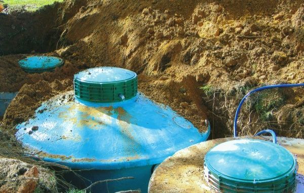 A blue septic tank is sitting in the dirt next to a bucket.