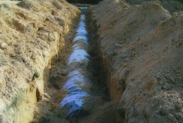 A pipe is being installed in the dirt in a trench.
