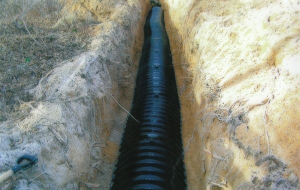 A black pipe is being installed in a trench.