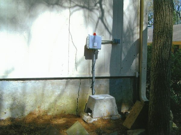 A white house with a tree in the background and a white box on the side of it.