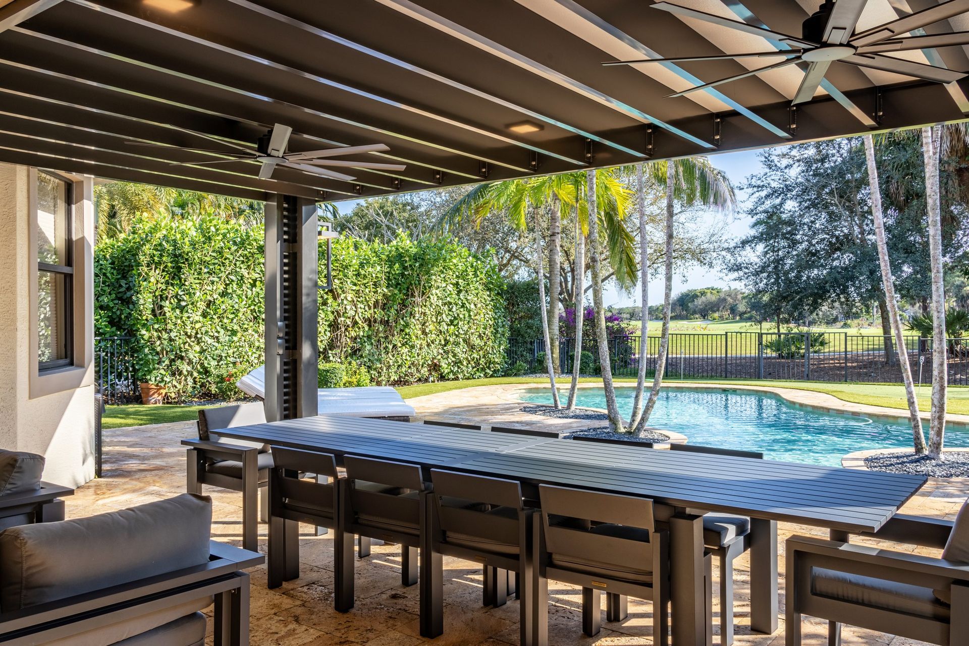 There is a large table and chairs under a canopy overlooking a pool.