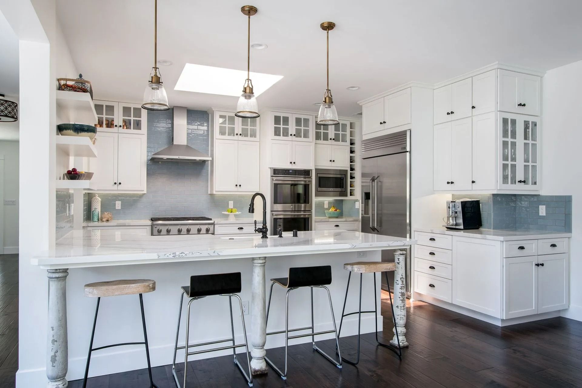 Modern white kitchen with a marble countertop island, pendant lights, and stainless steel appliances.