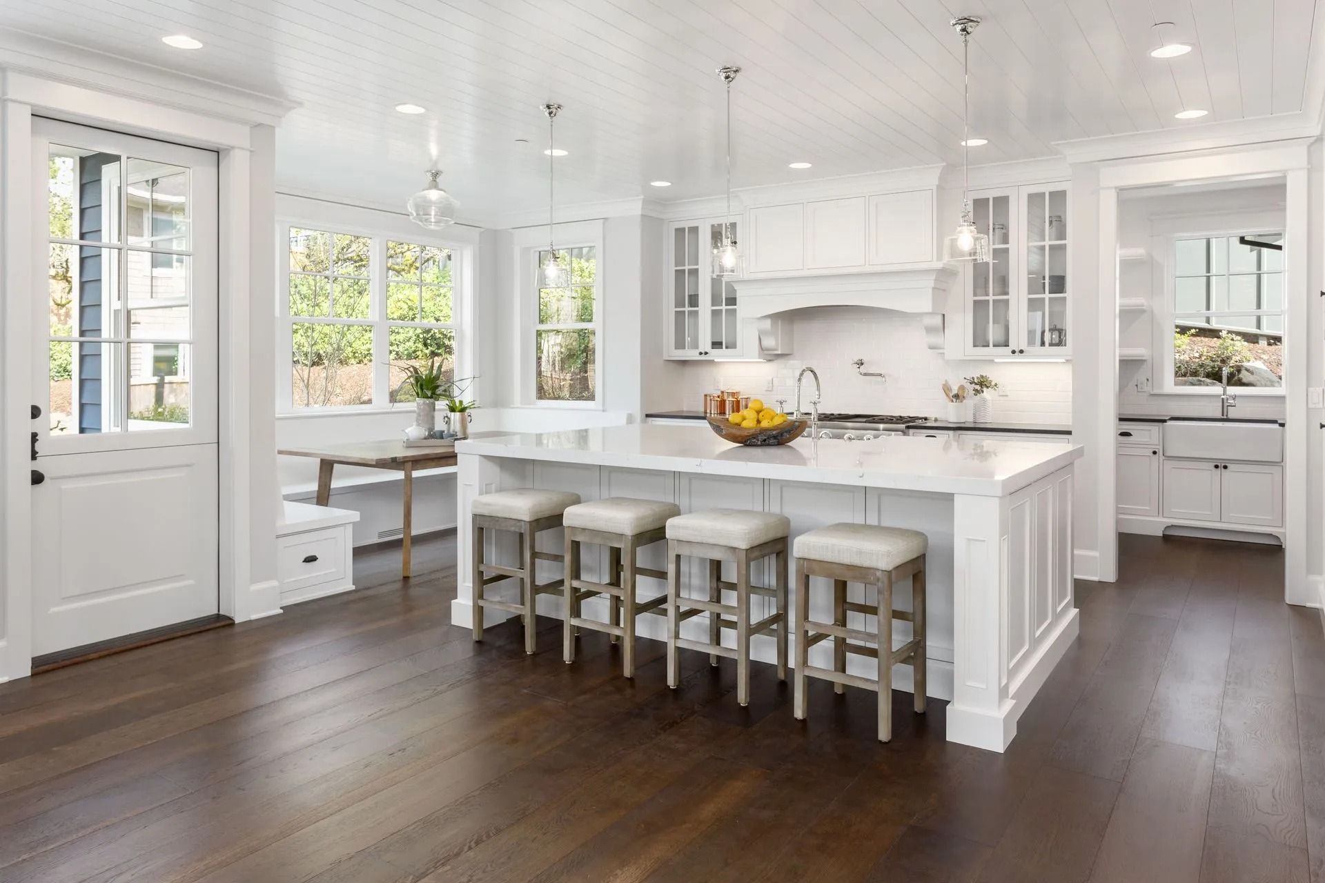 Bright white kitchen with a large island, stools, and dark wood floors.