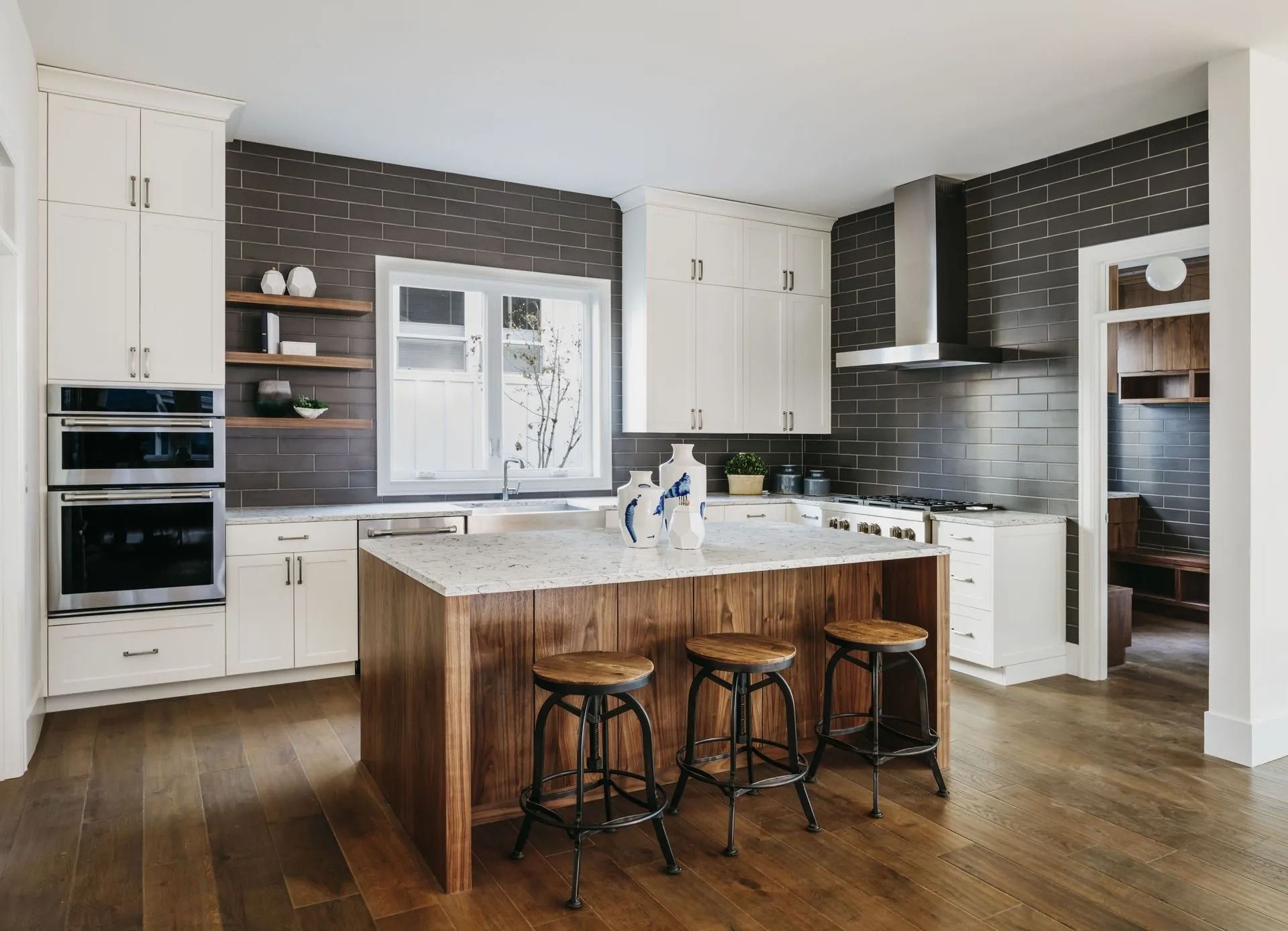 Modern kitchen with white cabinets, dark tiled backsplash, and wooden island with stools.