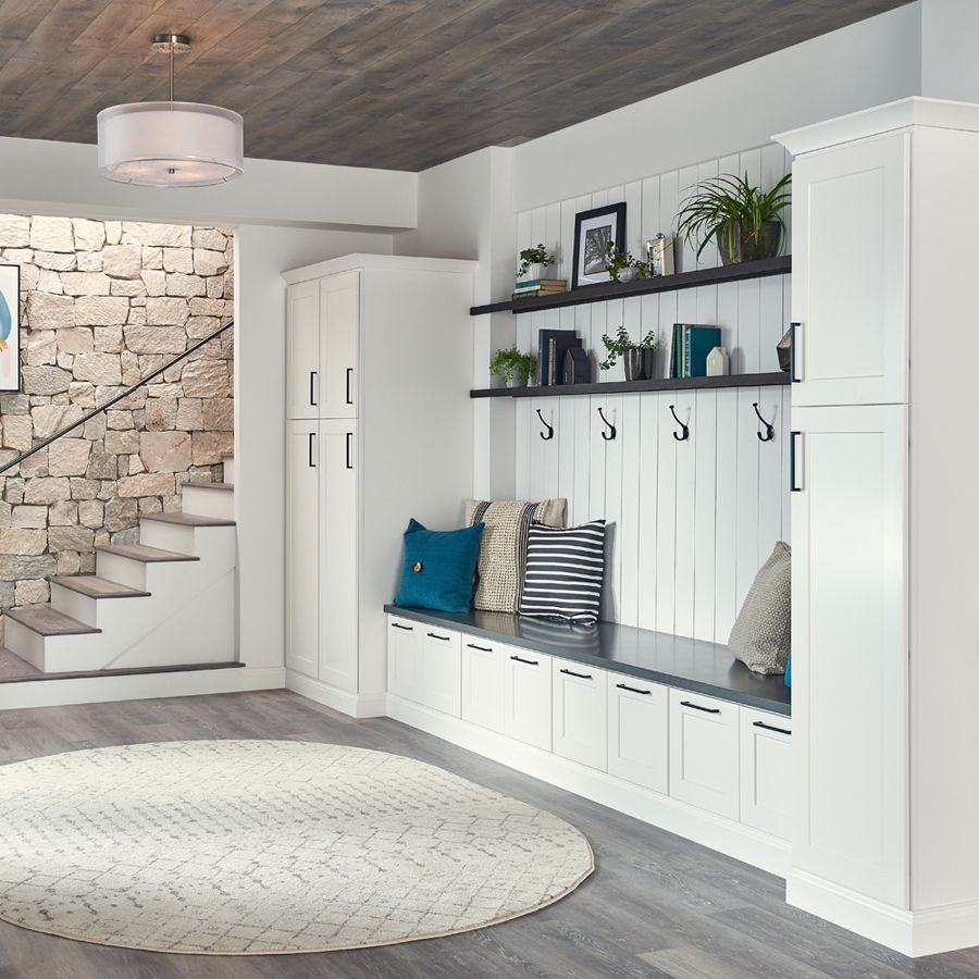 Entryway with built-in white cabinets, bench, shelves, and hooks. Stone staircase and round rug.
