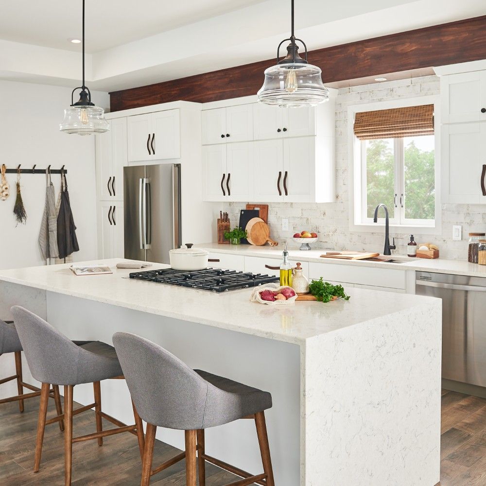 Modern white kitchen with island, gray stools, stainless steel appliances, and pendant lights.