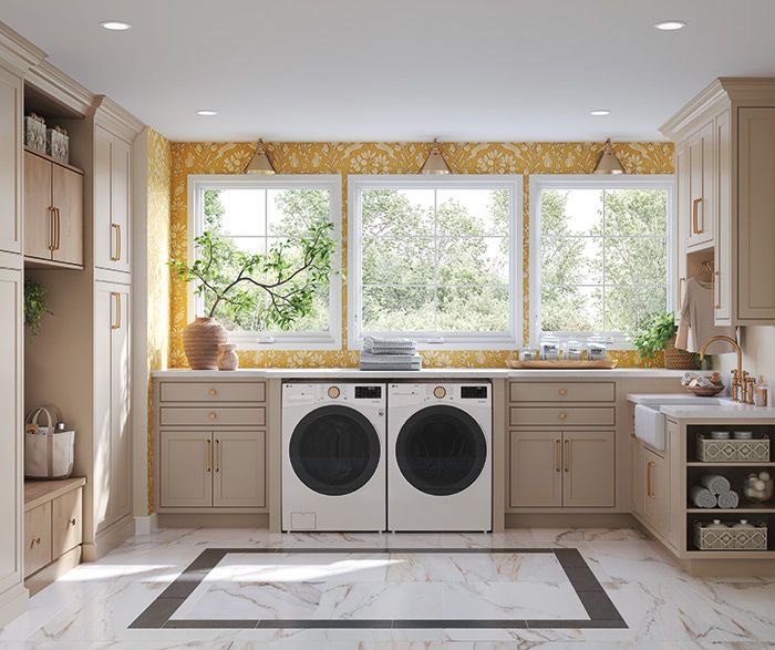 Laundry room with beige cabinets, washer/dryer, three windows with a yellow patterned backsplash, and marble floors.