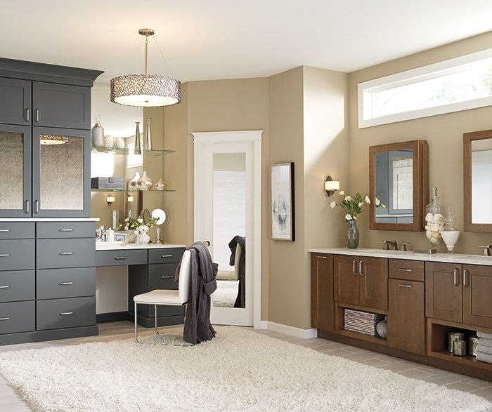 Spacious bathroom with gray and brown cabinets, vanity, mirrors, white door, and fluffy rug.