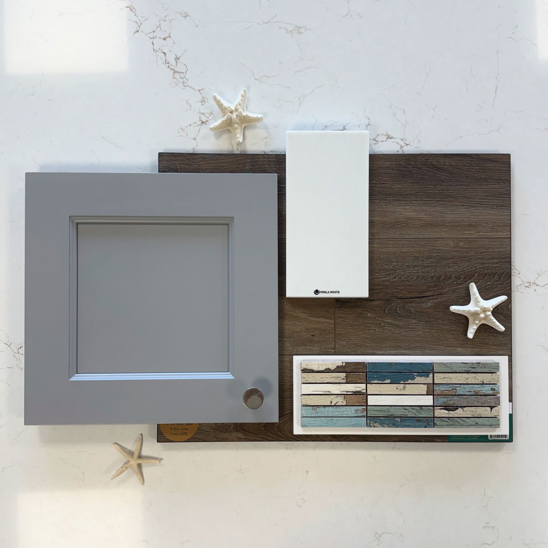 A flat lay of home interior samples: a gray cabinet door, white tile, weathered wood flooring, and coastal decor.