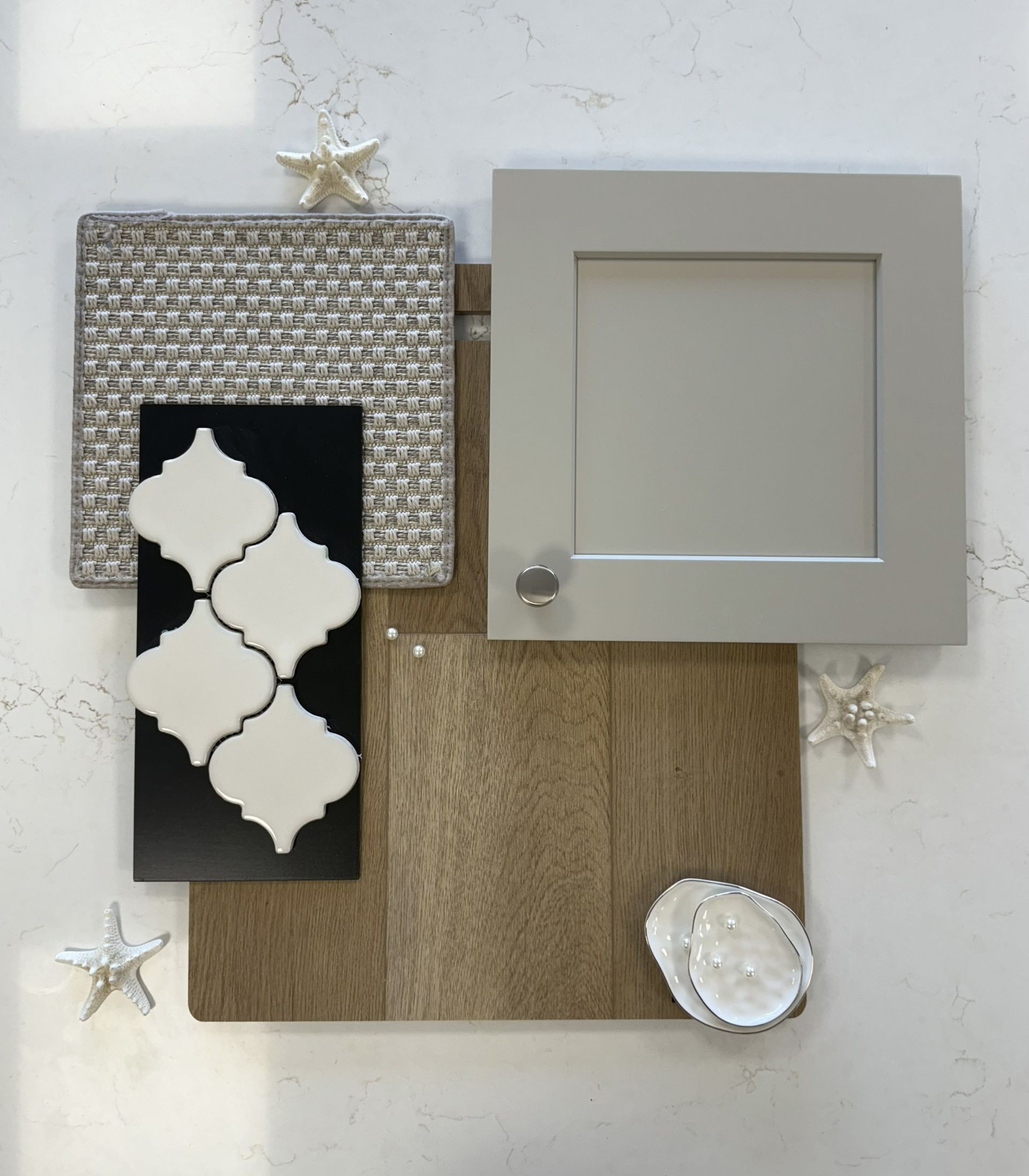 A interior design mood board featuring a gray cabinet door sample, wood floor plank, mosaic tiles, and decorative shells.