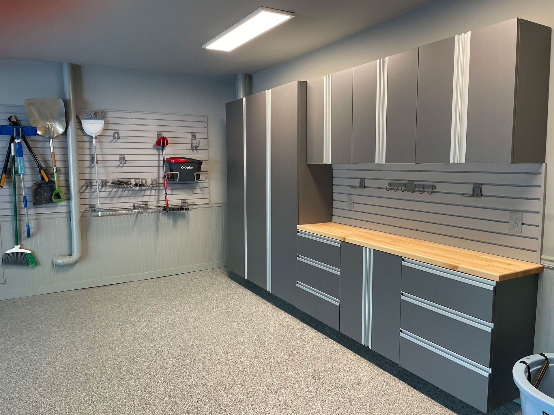 A modern garage with grey cabinets, a wooden countertop, a speckled floor, and wall-mounted storage panels.