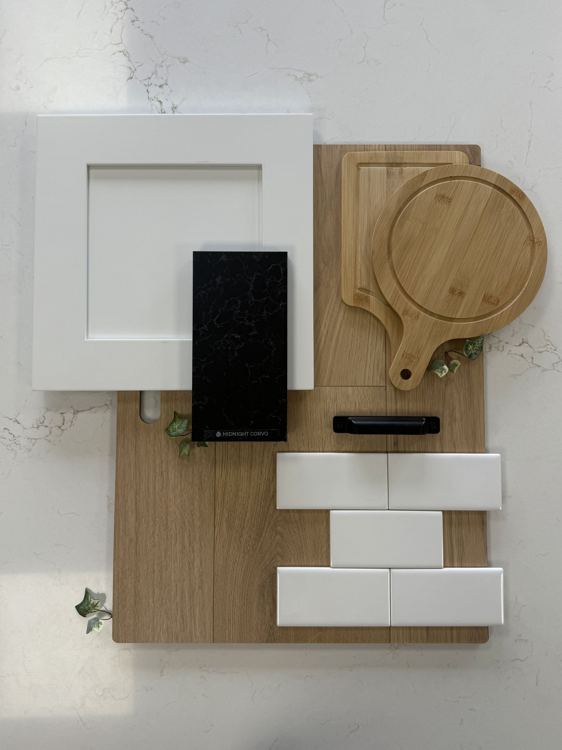 A flat lay of interior design samples, including white cabinetry, light wood, white subway tiles, and black hardware.