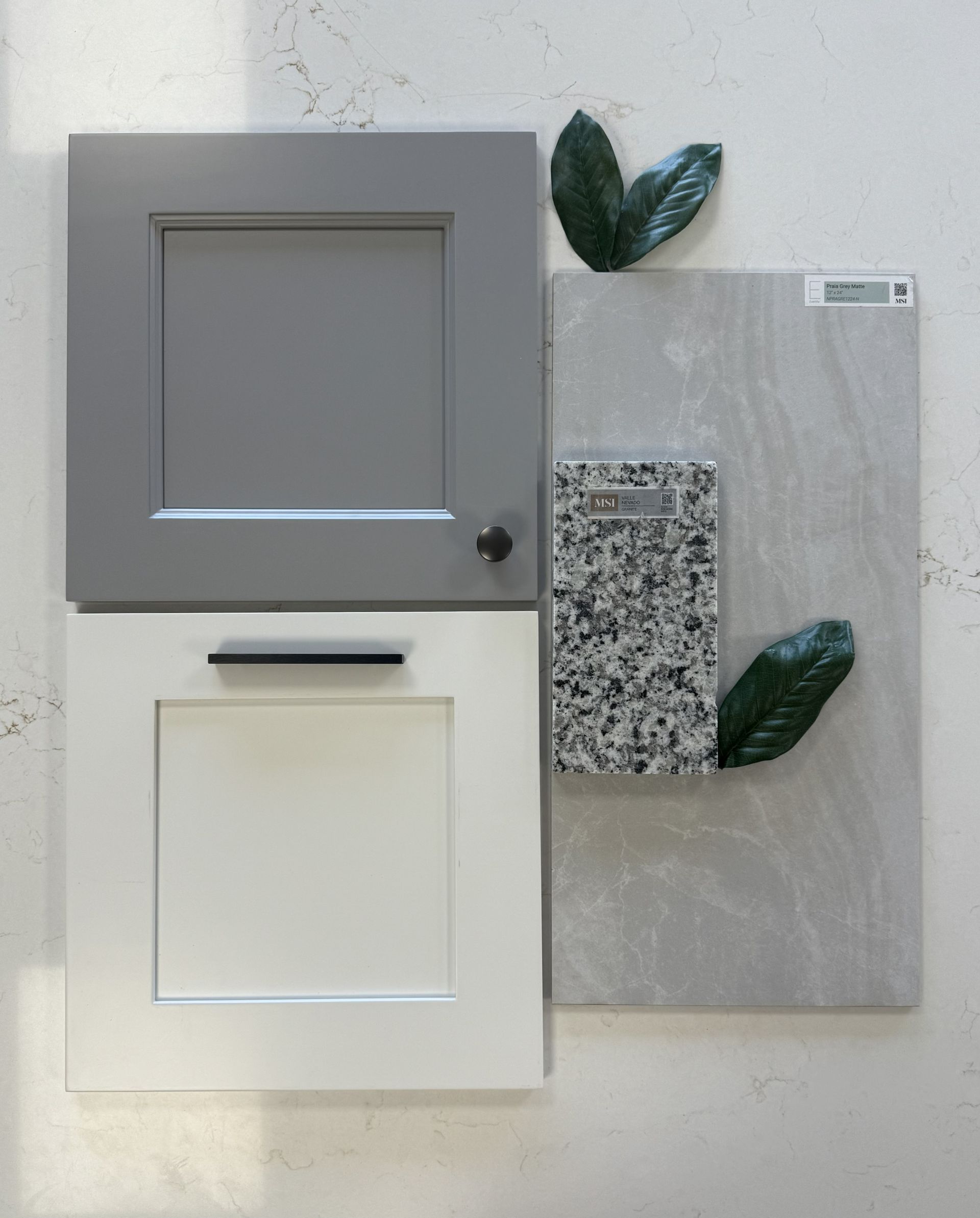 A mood board showing a grey and white cabinet door sample, a grey countertop slab, a granite sample, and two leaves.