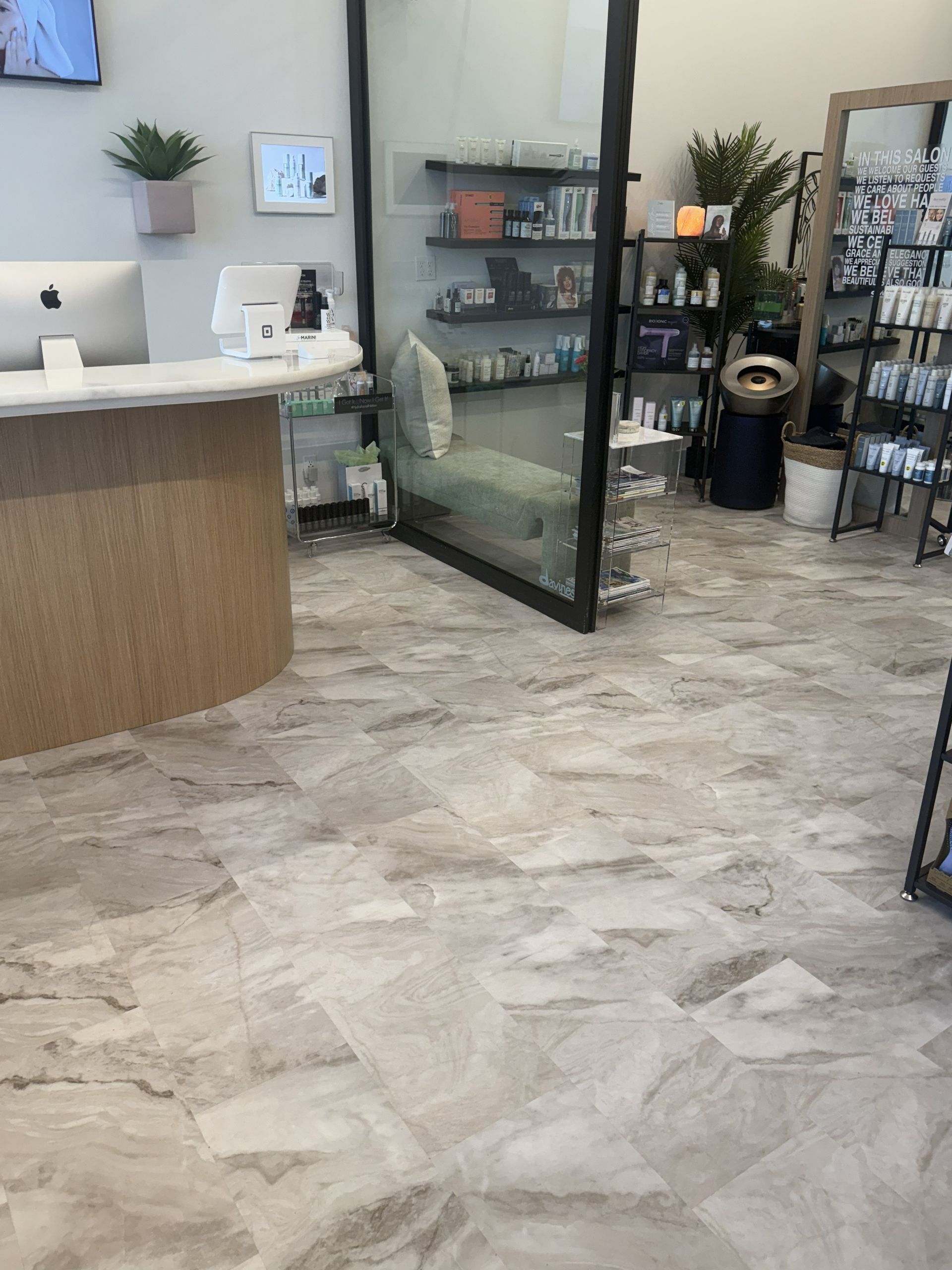 Modern office lobby with a curved front desk, marble-look tiled flooring, and retail product shelves behind glass.