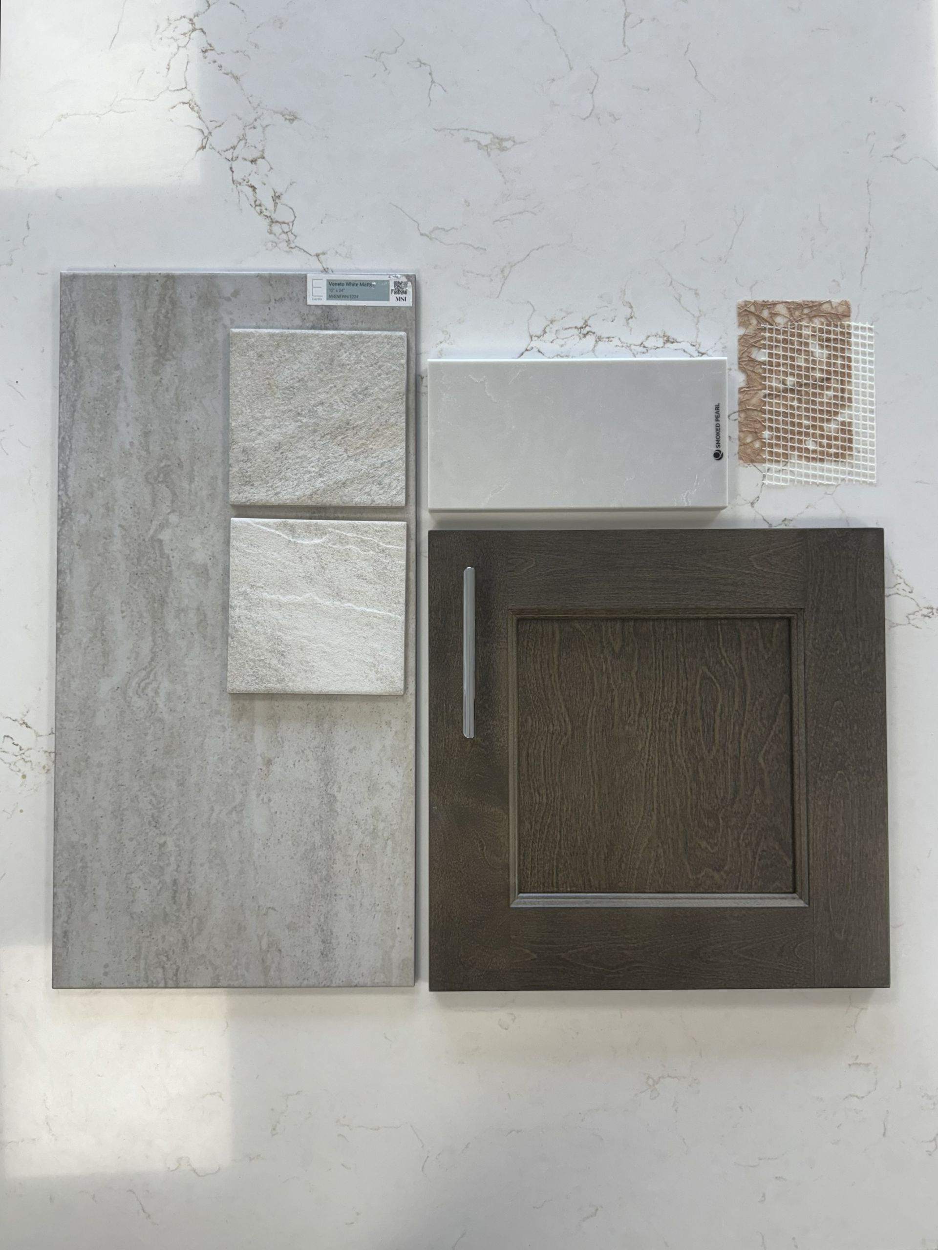 Design material samples including gray tiles, a dark wood cabinet door, a white block, and a small tile mosaic.