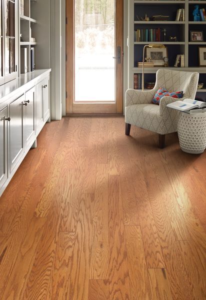 A cozy home library with light wood flooring, white built-in cabinets, a patterned armchair, and a wood-framed glass door.