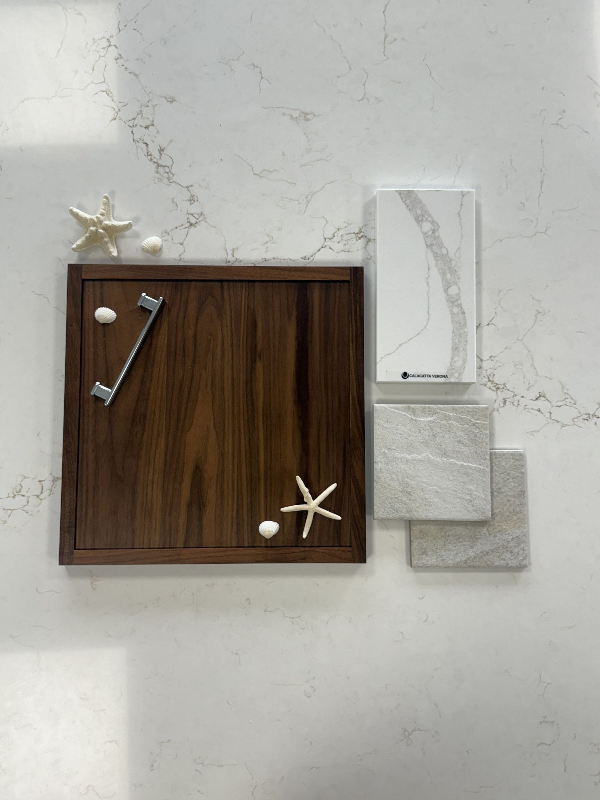 A wood cabinet sample with a silver handle, quartz stone, and textured tile pieces arranged on a white marble surface.