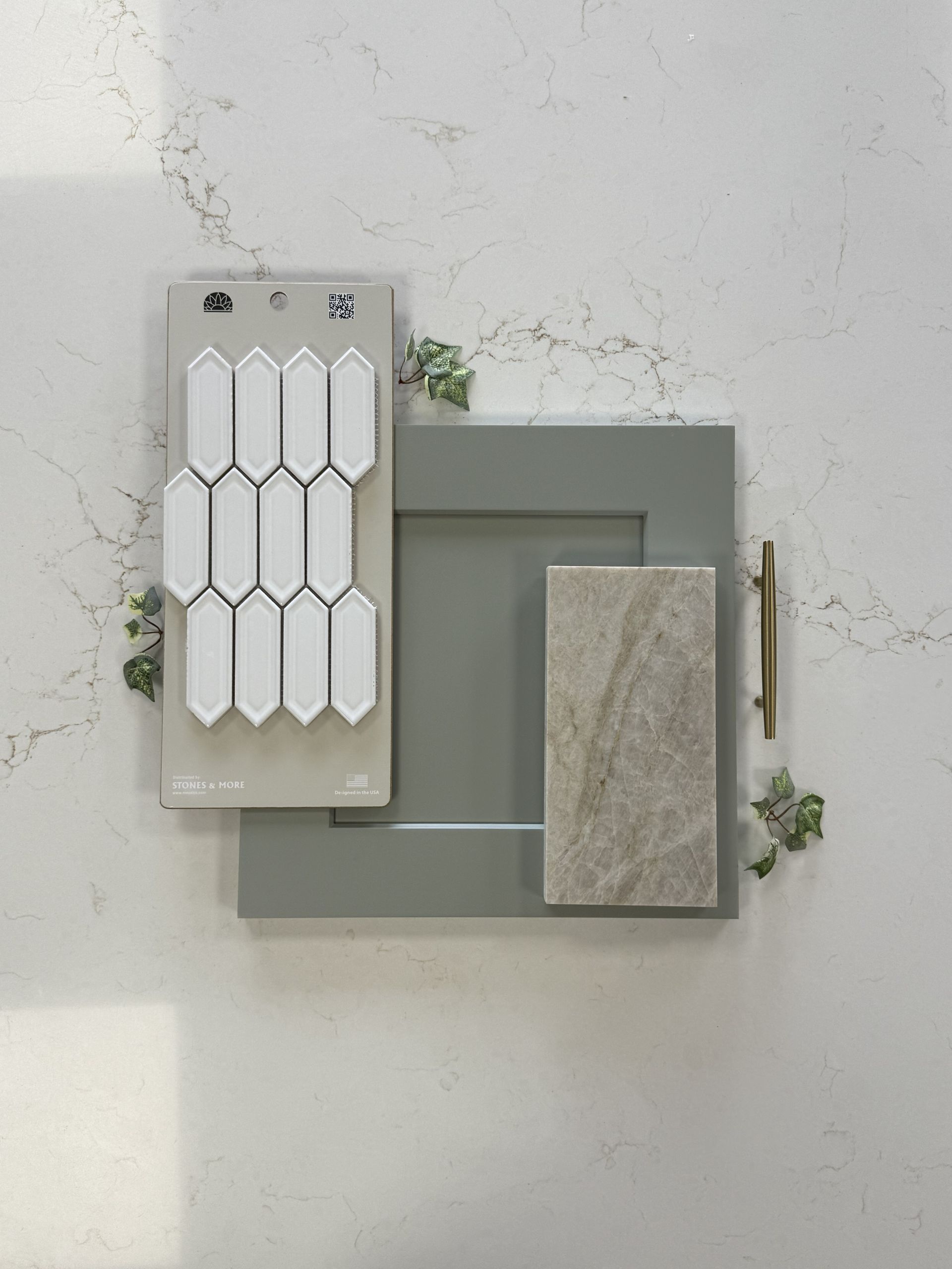 A design mood board with white picket tiles, a sage green cabinet sample, a textured stone tile, and a gold pull handle.