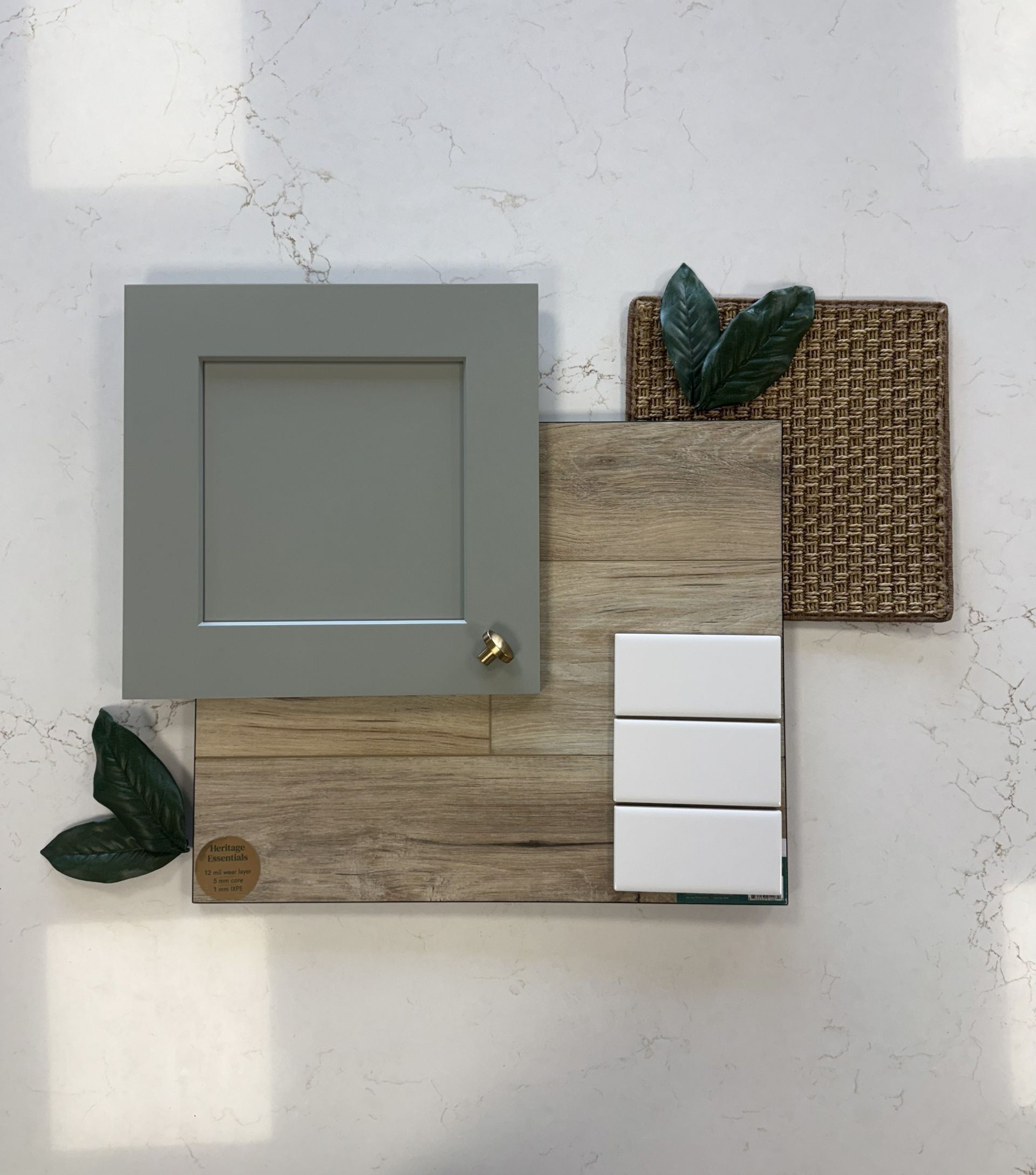 A design sample board featuring a grey cabinet door, wood-look plank, white tiles, and woven wicker on a white countertop.