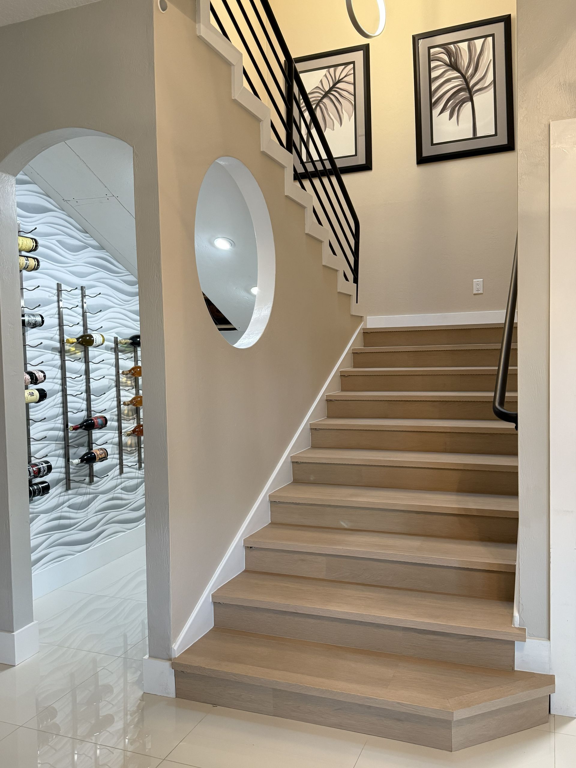 A staircase with wood-look steps and a black metal railing beside an arched entryway featuring a modern wine wall display.