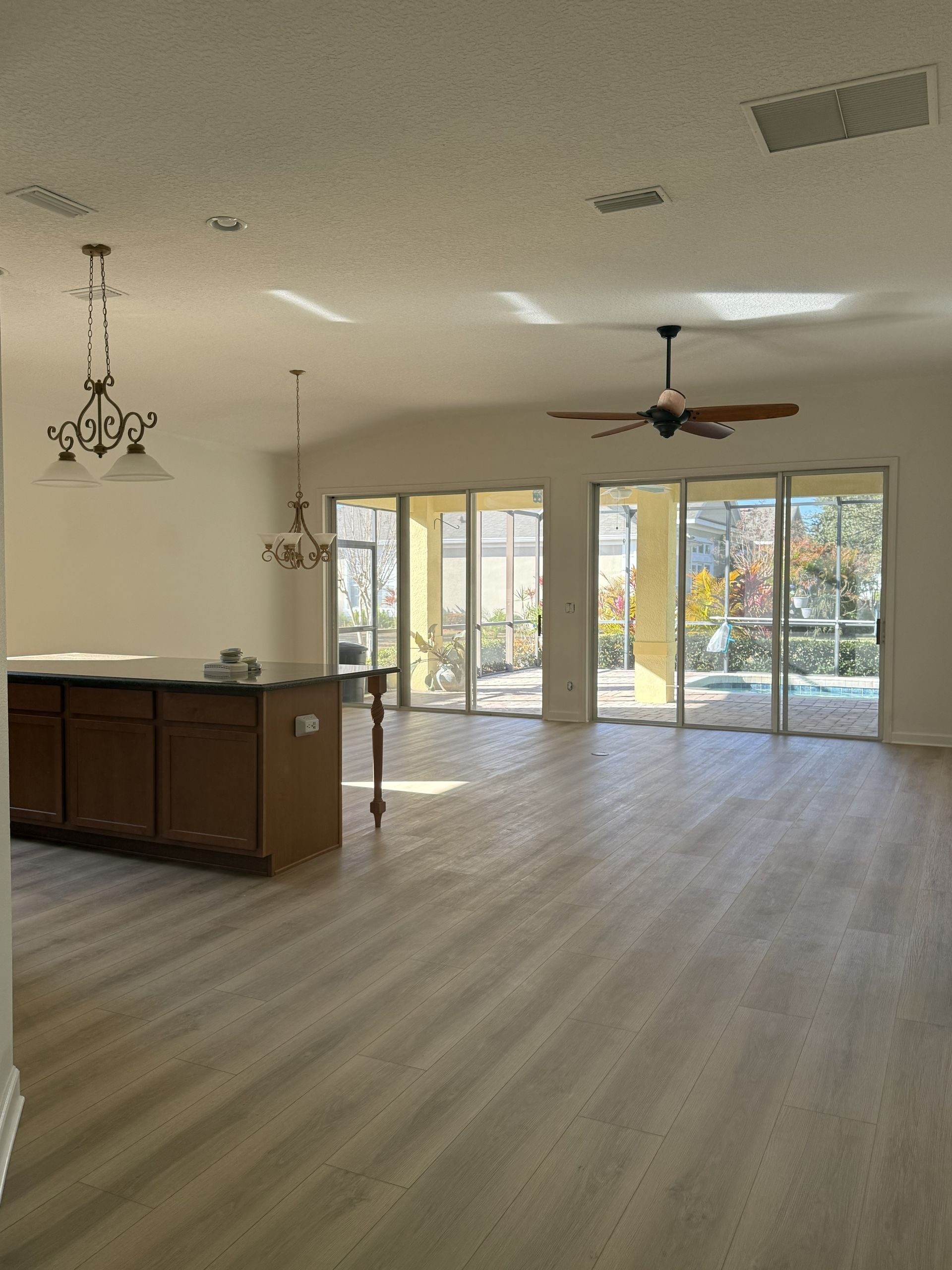 Open-concept room with wood-look flooring, a kitchen island, hanging lights, a ceiling fan, and large glass sliding doors.