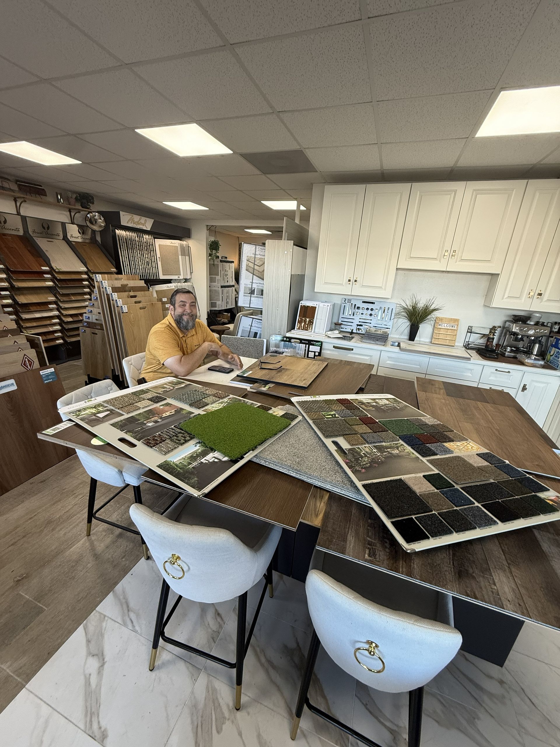 A person works at a table in a home design showroom, surrounded by flooring, tile, and cabinetry samples.