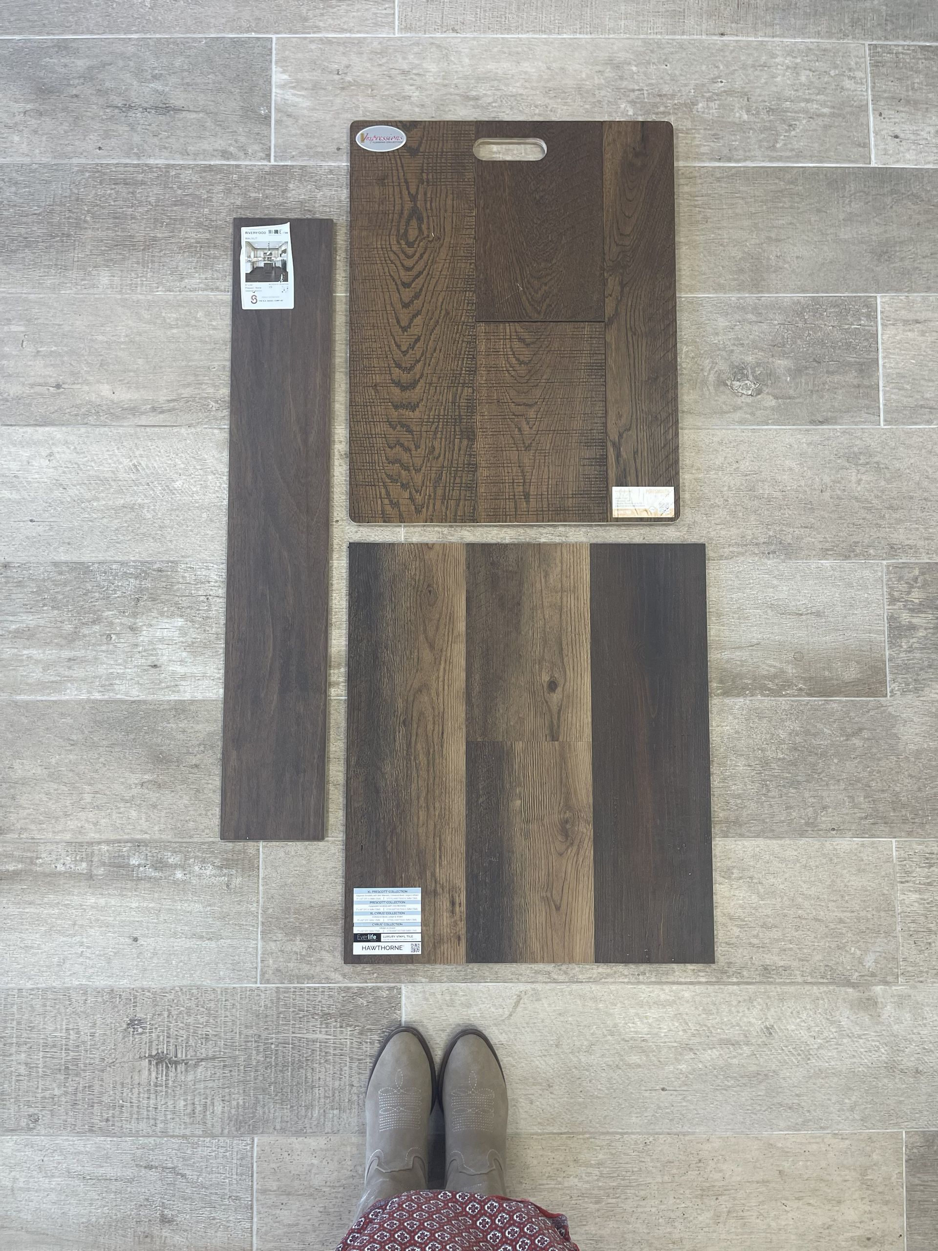 Three flooring samples in varying shades of dark wood are displayed on a light gray tile floor.