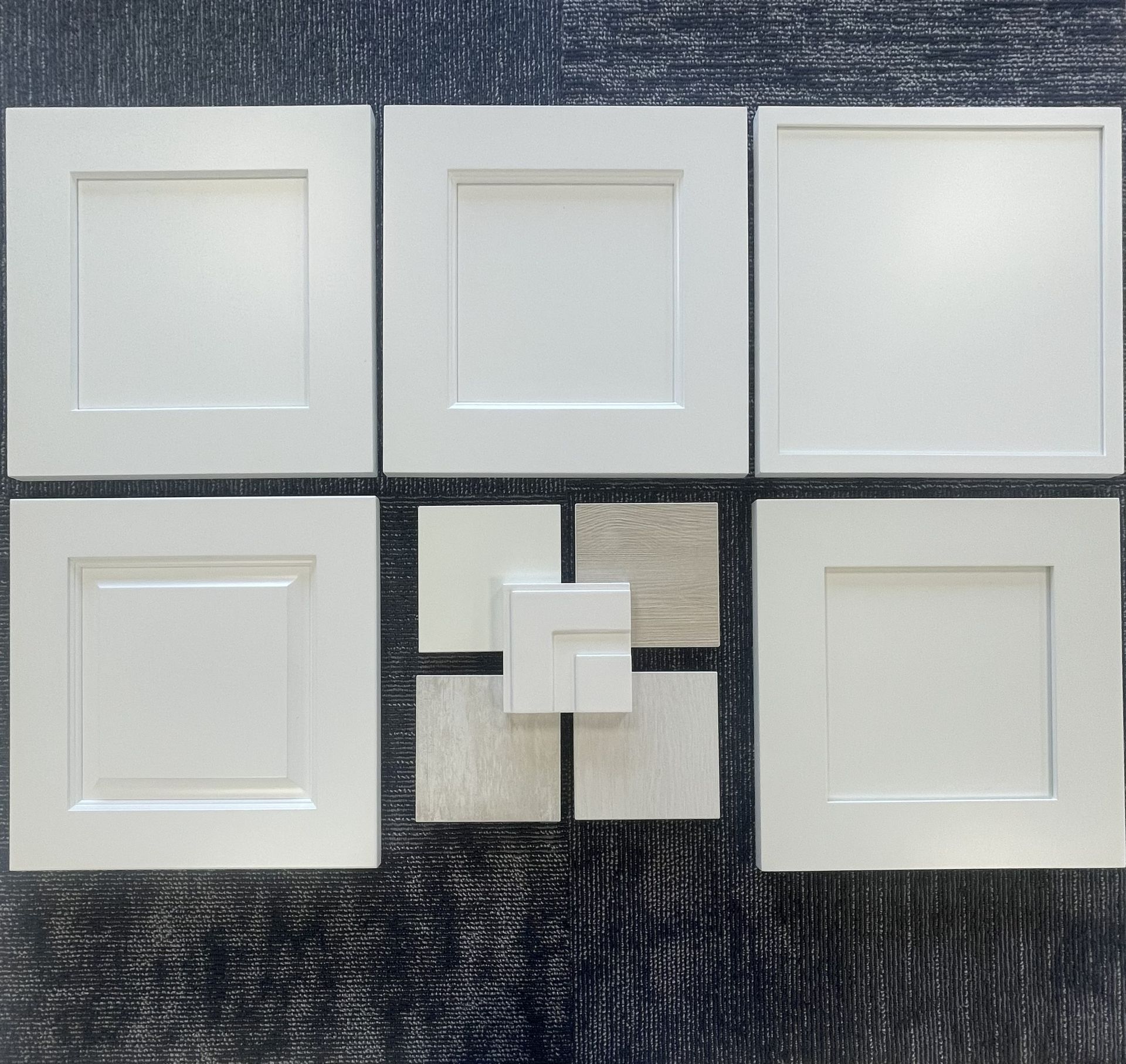 Display of five white cabinet door samples arranged around four small square material swatches on a dark blue background.