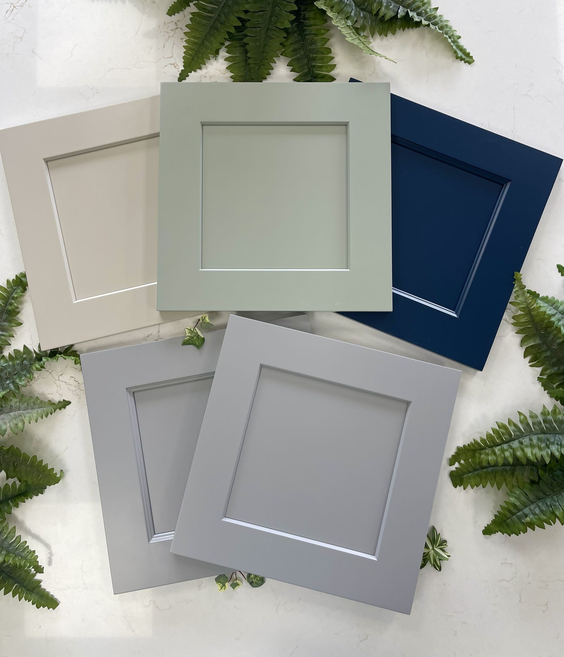 Five square cabinet door samples in beige, sage green, navy blue, light gray, and medium gray arranged on a white surface.