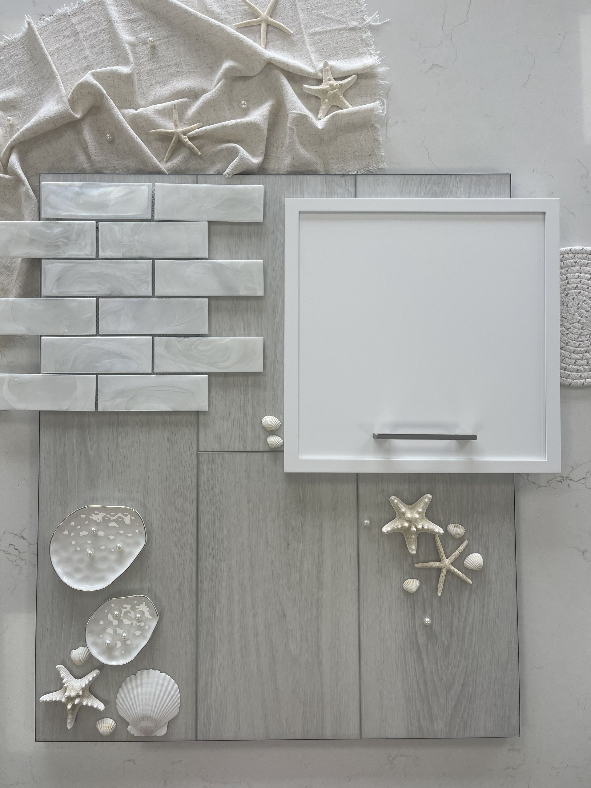 A design mood board with grey wood flooring, white subway tiles, a white cabinet door, and decorative shells and starfish.