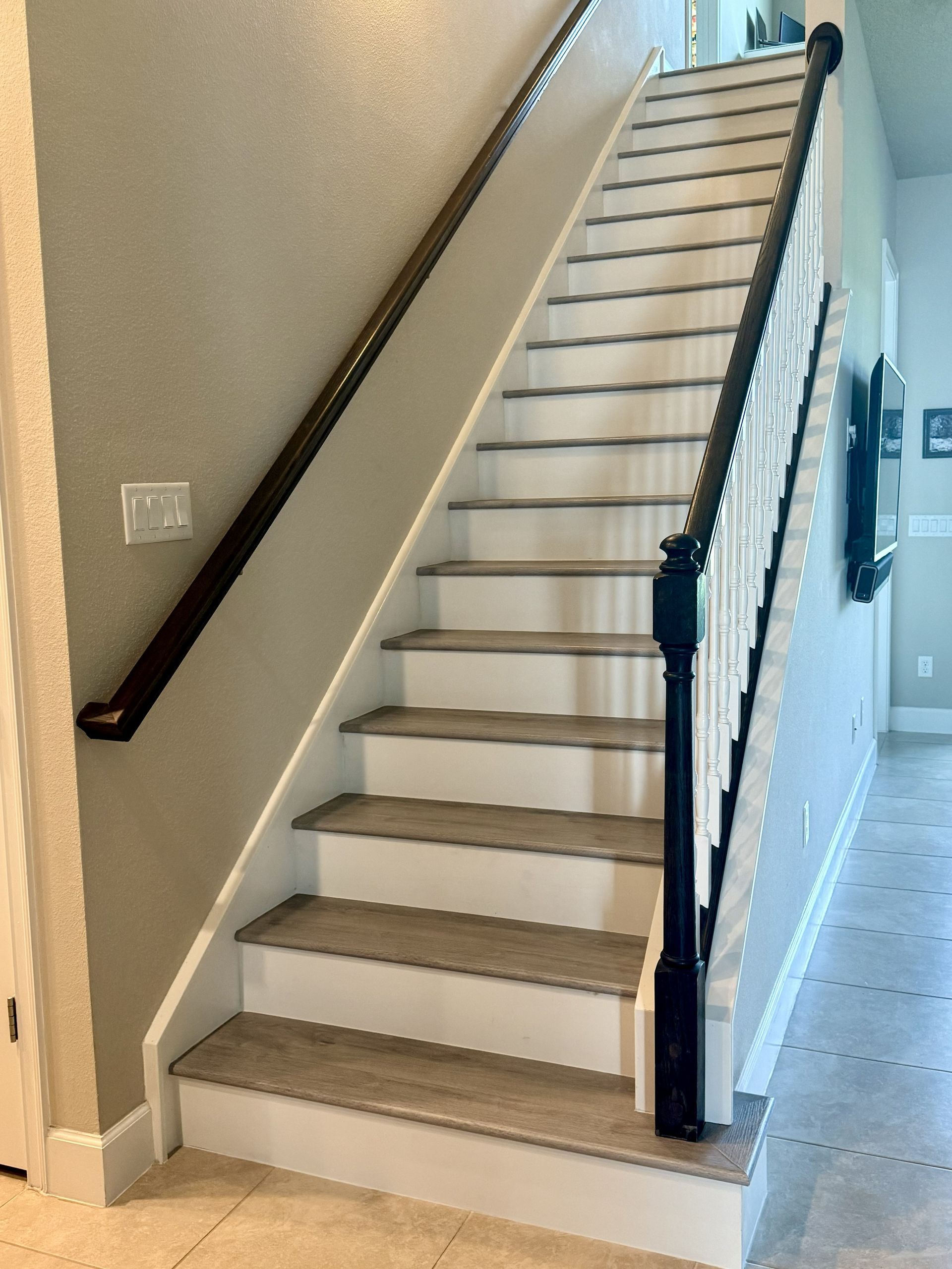 A straight staircase with wood-look treads, white risers, and black railings on both sides in a neutral-toned hallway.