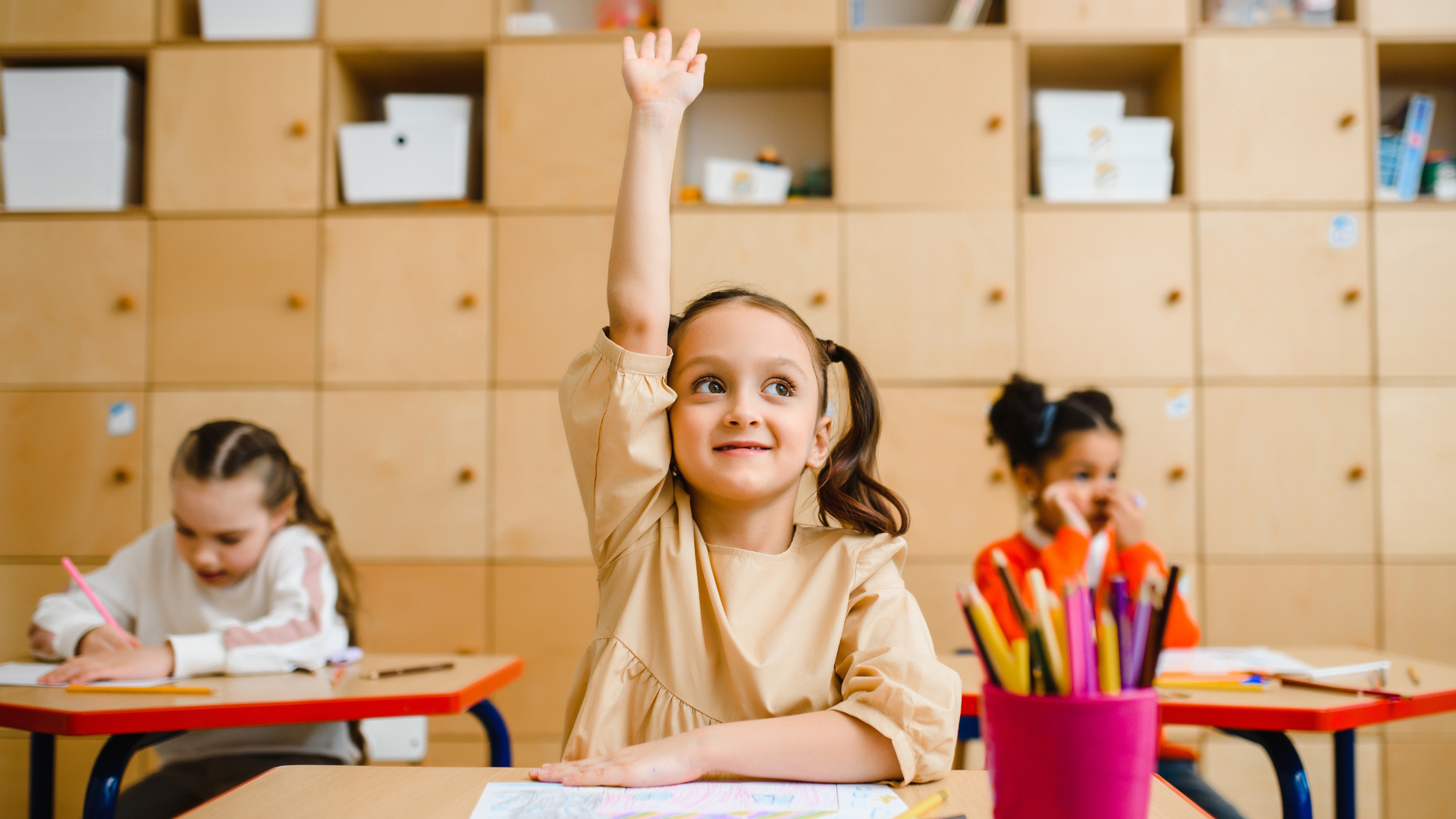 Smiling child raising hand in classroom, ready for back-to-school success