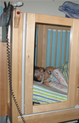 A child is laying in a wooden crib with an oxygen mask on their face