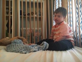 A little boy is sitting on a bed in a crib.