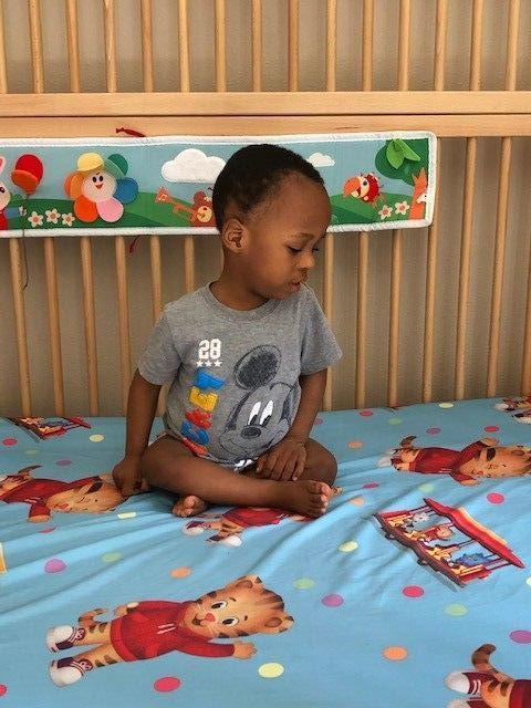 A baby is sitting on a bed with a mickey mouse shirt on