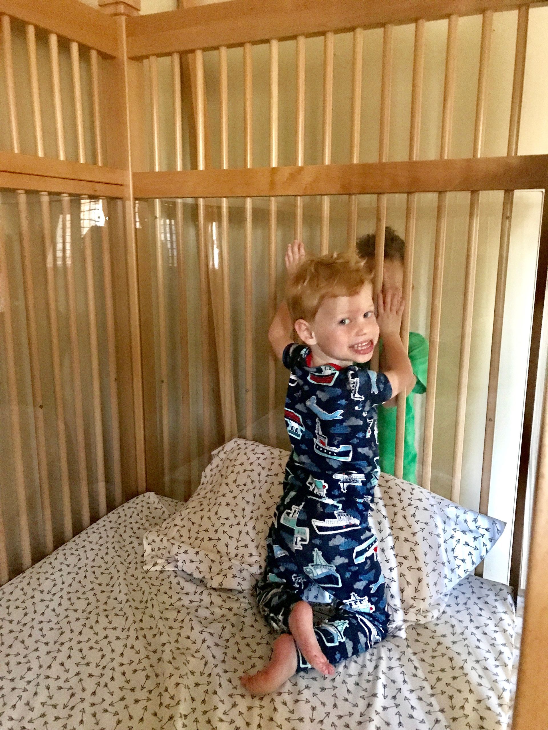 Two young boys are playing in a wooden crib.